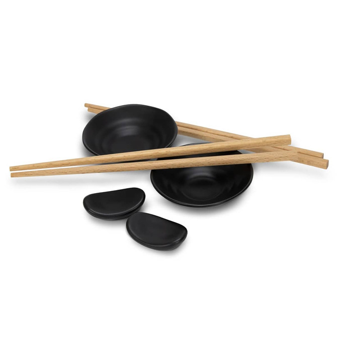 A sushi set featuring black dishes, two black sauce dishes, and wooden chopsticks arranged neatly.