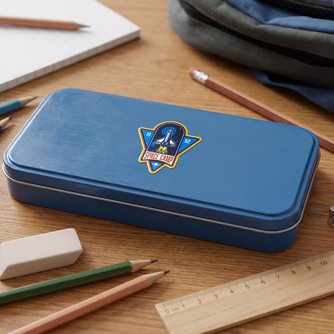 A blue pencil case with a logo, surrounded by pencils, a ruler, and a notebook on a wooden surface.