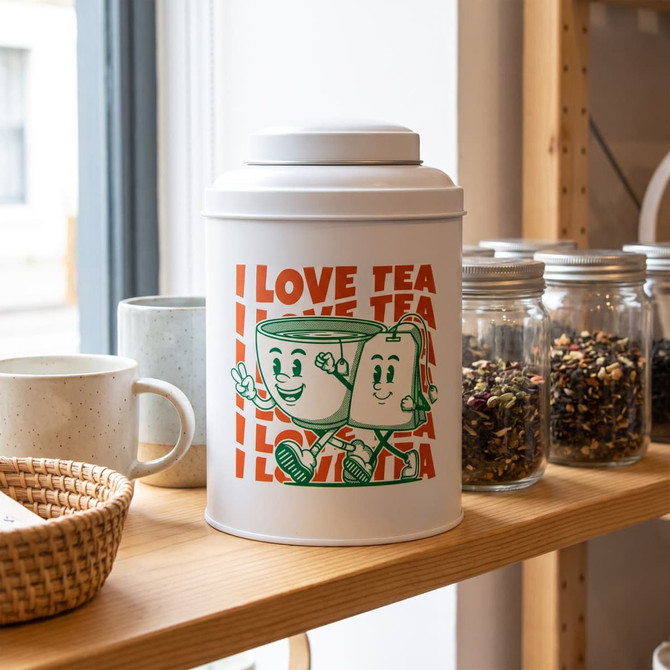 A tea canister with a playful design featuring cartoon cups, in white and green, on a wooden shelf with jars and cups.