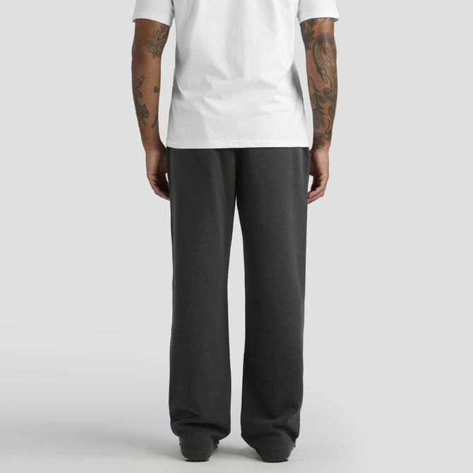 A person with tattoos stands wearing relaxed, faded cuffless track pants in charcoal grey, paired with a white t-shirt.