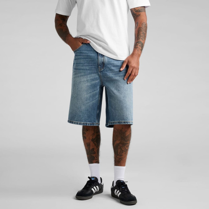 A pair of blue denim shorts featuring a relaxed fit, worn by a person with tattoos and black sneakers.