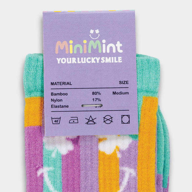 Colourful knitted socks in purple, yellow, and green, featuring a floral design, with a label indicating material details.