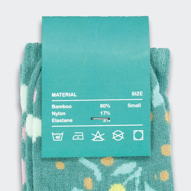 A pair of teal knitted socks featuring a floral pattern, with a label indicating material and size.