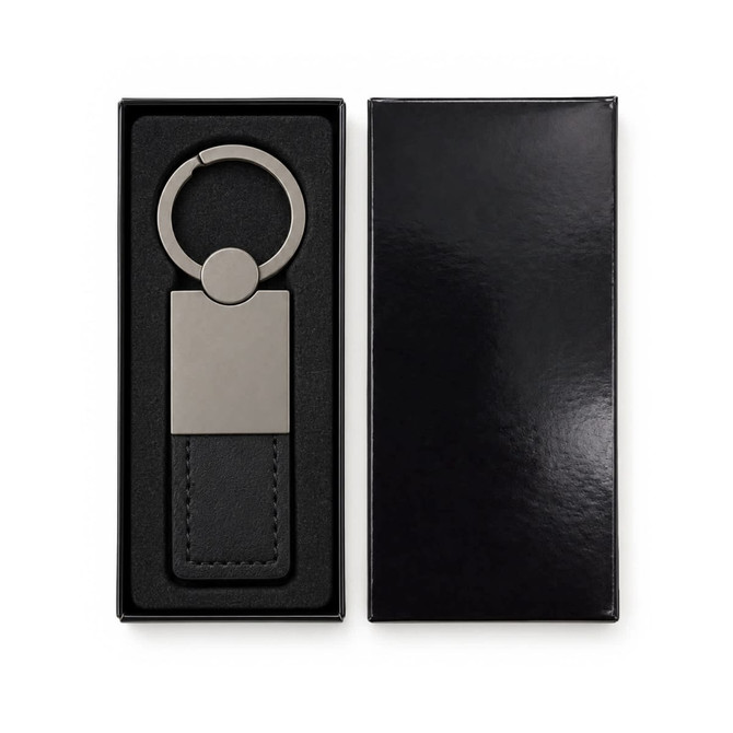 A metallic keytag with a leather strap in a black gift box, featuring a smooth surface and circular keyring.