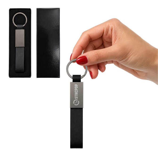 A keytag with a sleek black strap and metallic ring, presented in a black box, held by a hand with red nails.