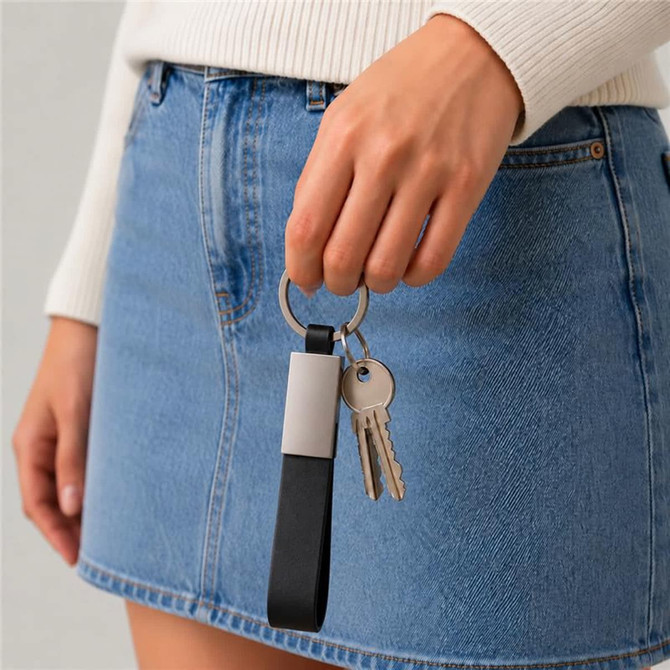 A hand holding a black and grey keytag with a keyring, against a backdrop of a denim skirt.