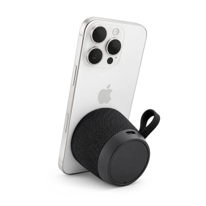 A black portable speaker is attached to a smartphone, featuring a textured surface and a strap.