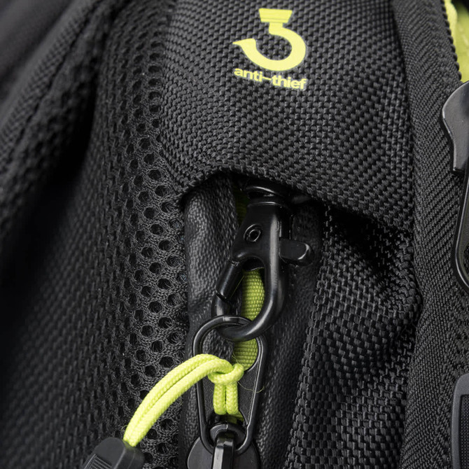 A close-up of a black backpack feature with a green zipper and an anti-thief clip. It has a textured fabric.