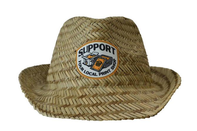 A straw fedora hat in a natural tan colour with a logo on the front.