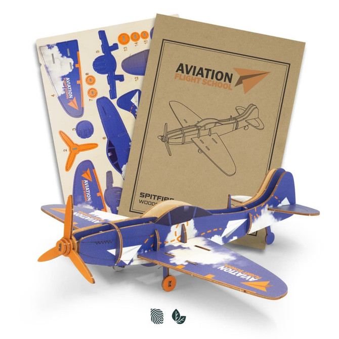 A wooden model of a Spitfire aircraft in blue and orange, with assembly sheets and instructional guides in the background.