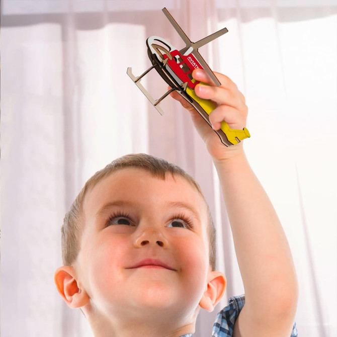 A child holding a brightly coloured wooden helicopter model with yellow and red details.