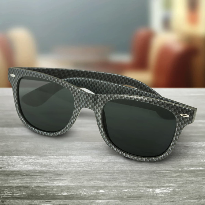 Premium sunglasses in carbon fibre design with dark lenses, featuring a logo, placed on a wooden surface.