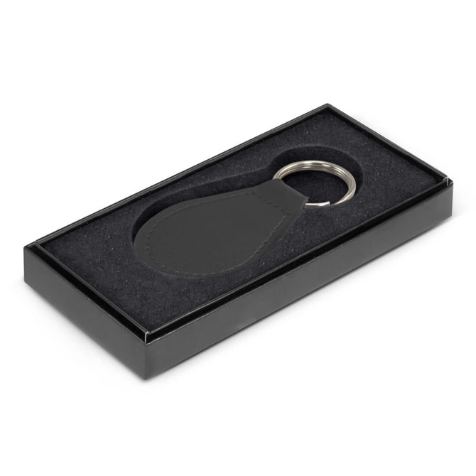 A round leather key ring in a black gift box with a plush interior. The key ring has a silver metal attachment.