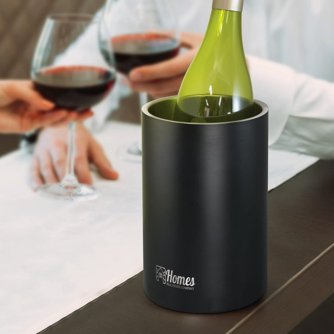 A black vacuum wine cooler holds a green wine bottle, with wine glasses in the background. The cooler has a logo.