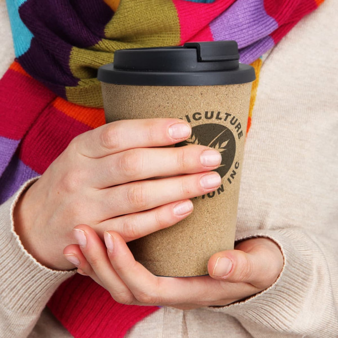 A drink bottle with a cork-like finish and a black lid, held by a person wearing a multicoloured scarf.