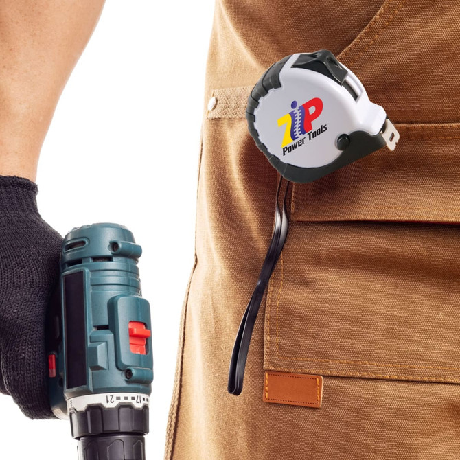 A retractable tape measure in black and white attached to a work apron, with a power tool in hand.