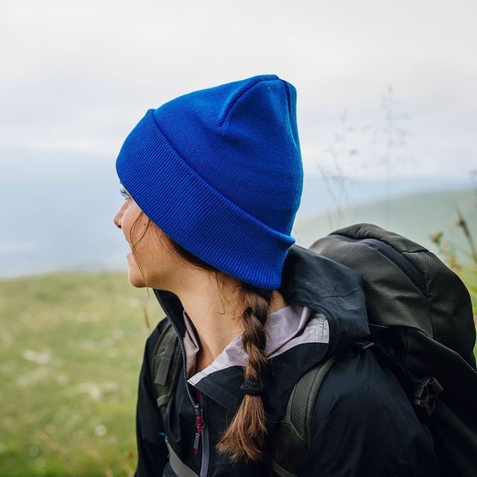 A blue beanie worn by a woman outdoors, with a backpack visible on her back and a scenic background.