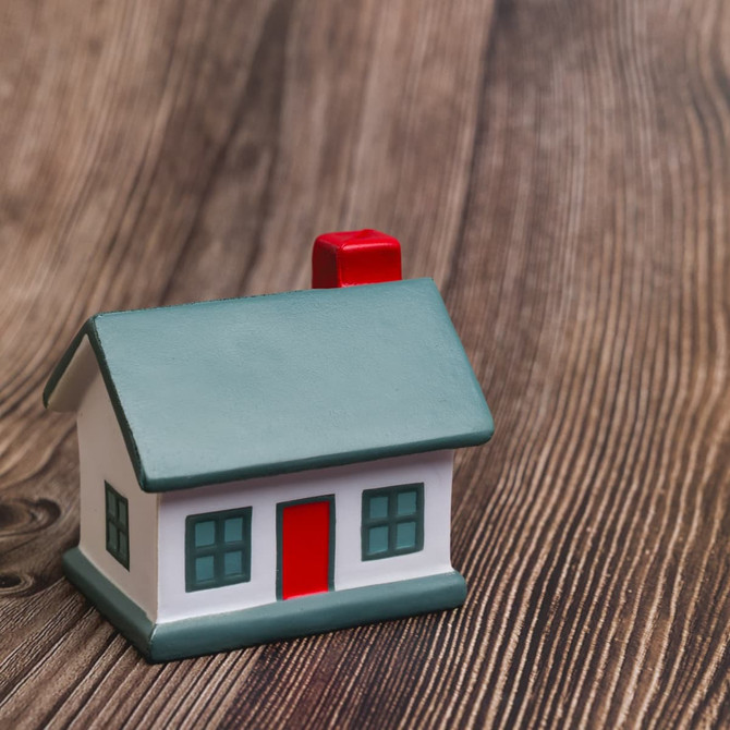 A small, colourful house stress reliever with a green roof, red chimney, and white walls, set on a wooden surface.
