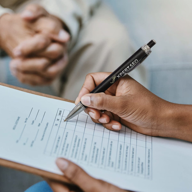 A black metal pen with a clip, being held above a clipboard with a checklist on it. The pen features a logo.
