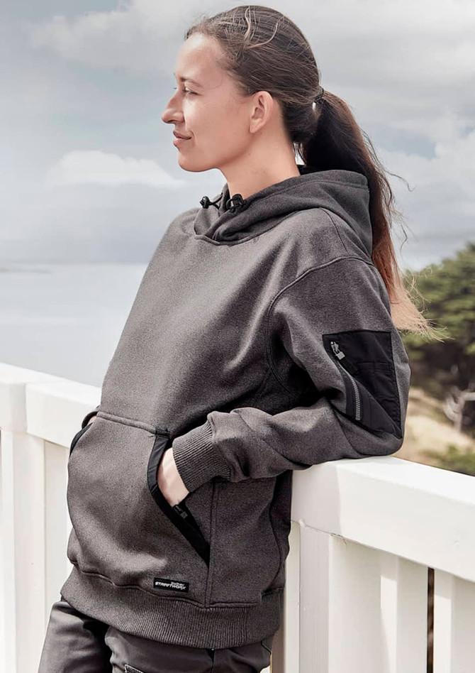 A unisex water-resistant hoodie in dark grey, featuring a front pocket and logo, worn by a woman outdoors.