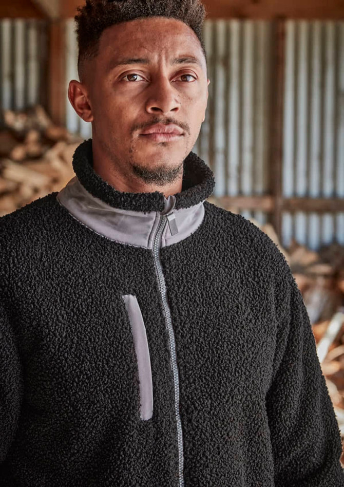 A man models a black full zip Sherpa fleece work jumper with grey detailing and a logo on the chest.