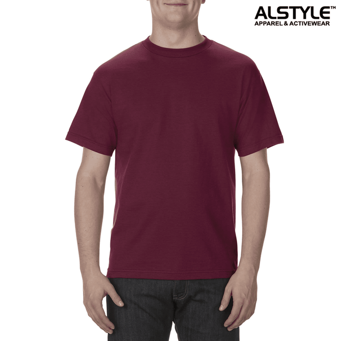 A unisex heavyweight cotton T-shirt in burgundy, featuring a logo. The model stands casually, wearing jeans.