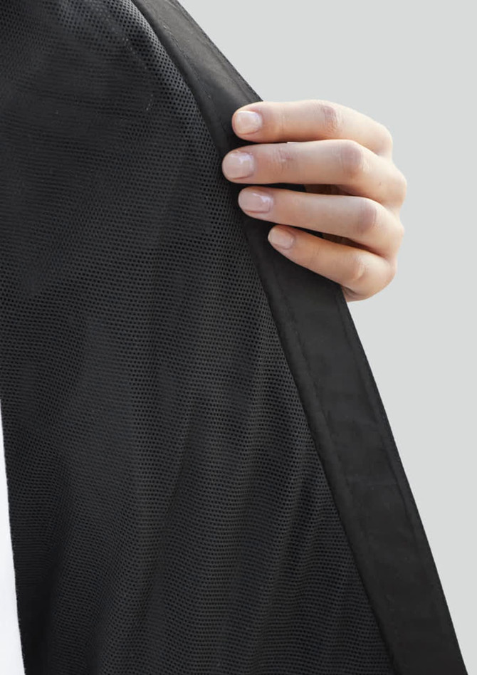 A close-up of a hand holding the edge of a black women's rain jacket with a textured finish.