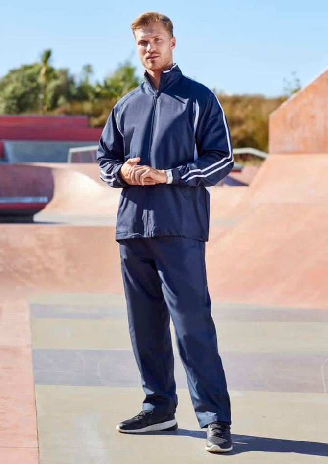 A model stands in a skate park wearing navy unisex track pants, paired with a matching zip-up jacket and sneakers.