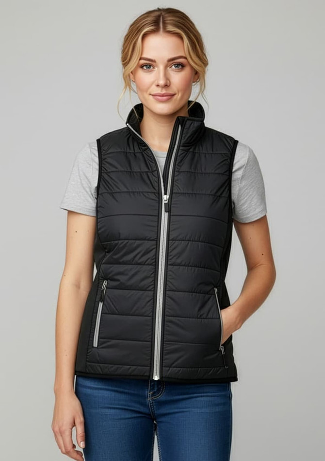 A woman is wearing a black puffer vest with a zip front, paired with a grey t-shirt and blue jeans.