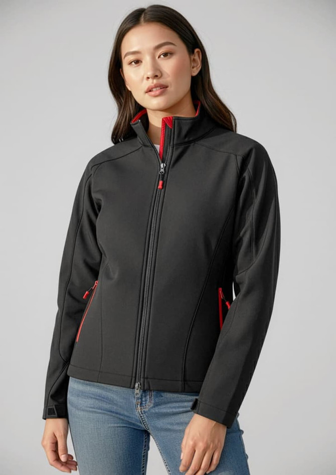 A black soft shell jacket with red accents, featuring a high collar and zippered pockets, modelled by a woman.