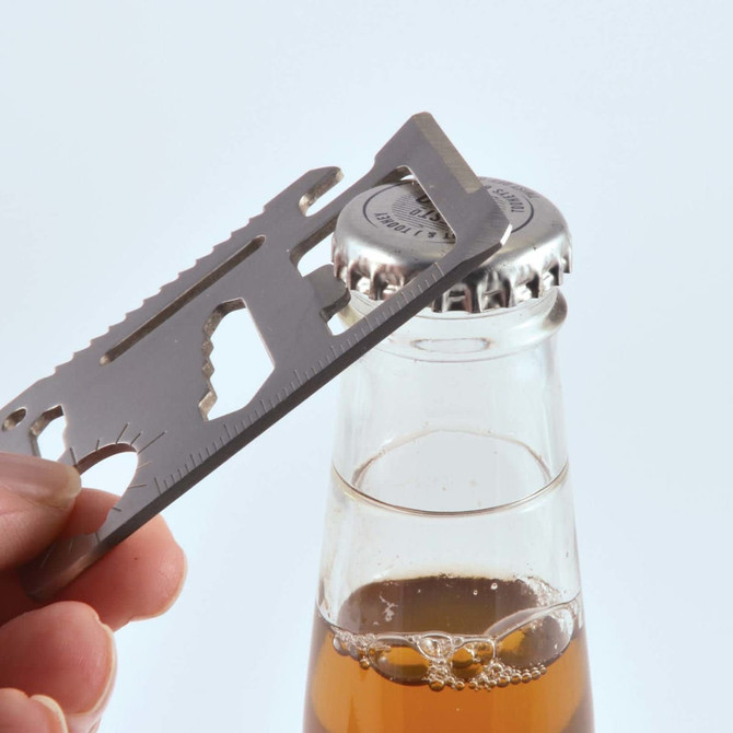 A stainless steel multi-tool is being used to open a bottle cap, with a drink bottle visible in the background.