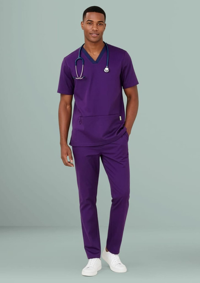 A male model wearing a purple scrub top and matching pants, with a stethoscope around his neck.