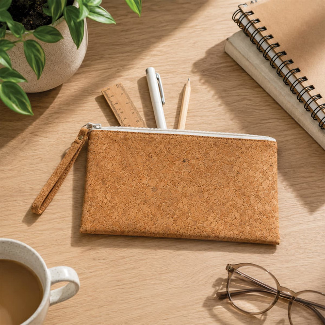 A cork pencil case with a zip closure, surrounded by pens, a ruler, a notebook, and a cup of coffee.