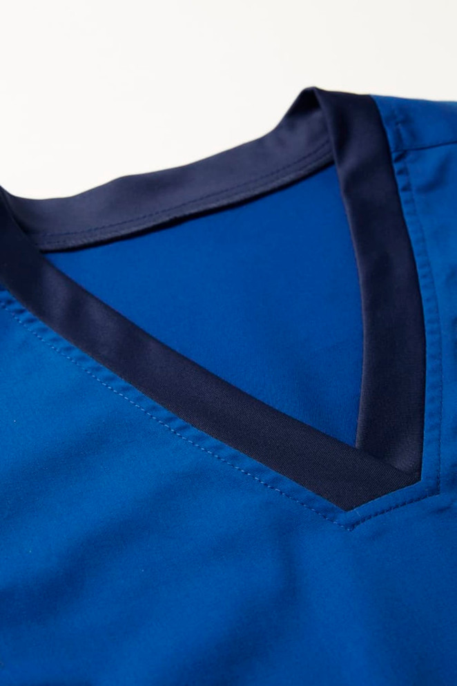 A blue scrub top with a navy contrast V-neck collar and smooth fabric texture. Features a logo.