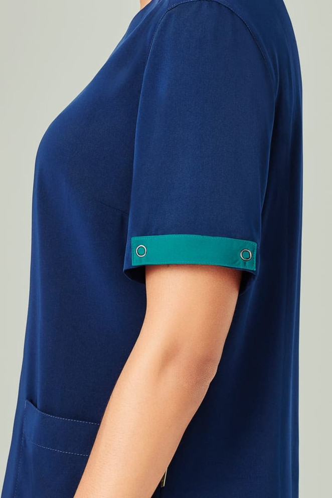 A navy blue unisex scrub top with short sleeves featuring a teal accent on the cuffs. It has a pocket on the front and a logo.