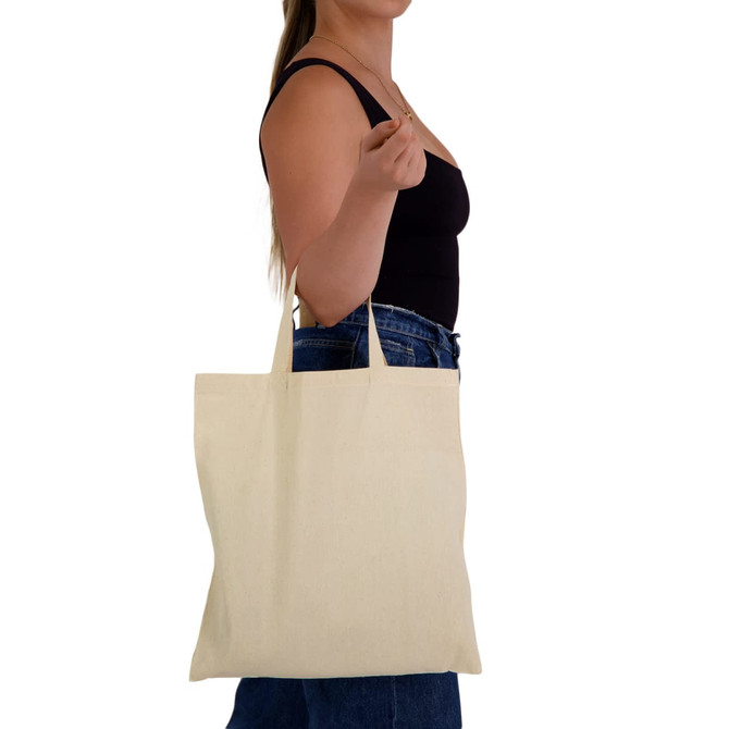 A cream-coloured tote bag with short handles held by a person, featuring a logo.