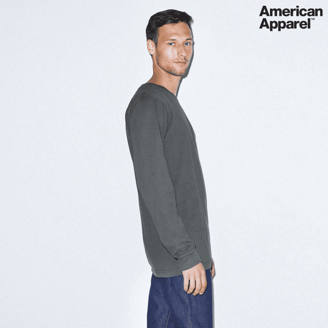 A grey long sleeve fine jersey T-shirt by American Apparel displayed on a model. The shirt has a logo.