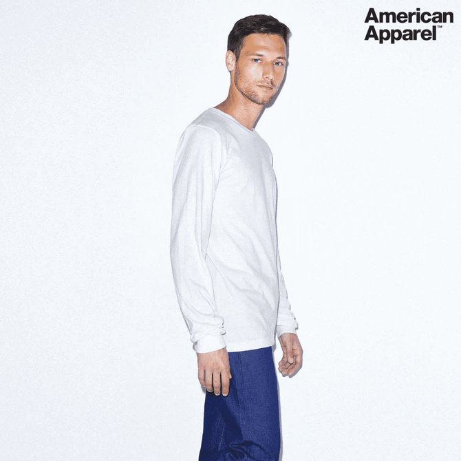 A man wearing a white long sleeve fine jersey t-shirt paired with dark blue jeans, featuring a logo.