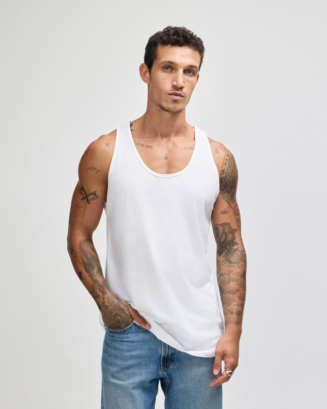 A model wearing a white unisex fine jersey tank top, paired with blue jeans, showcasing a minimalist style.