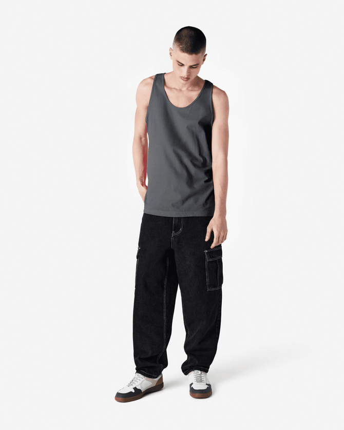 A grey unisex tank top displayed on a model wearing black cargo pants and shoes. The tank features a brand logo.