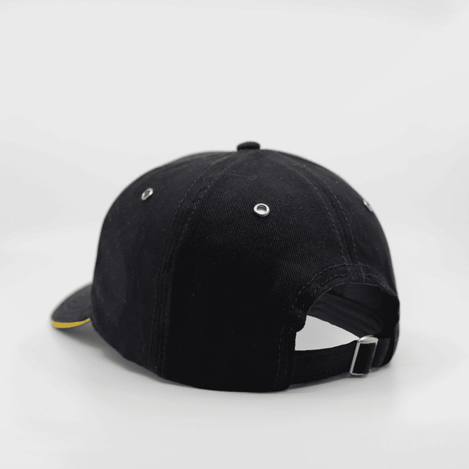 A black cap with a yellow under-brim and a metal adjuster at the back. It features ventilation eyelets and a logo.