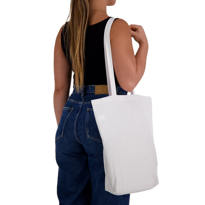 A white cotton tote bag with long handles is being carried by a person wearing a black top and blue jeans.