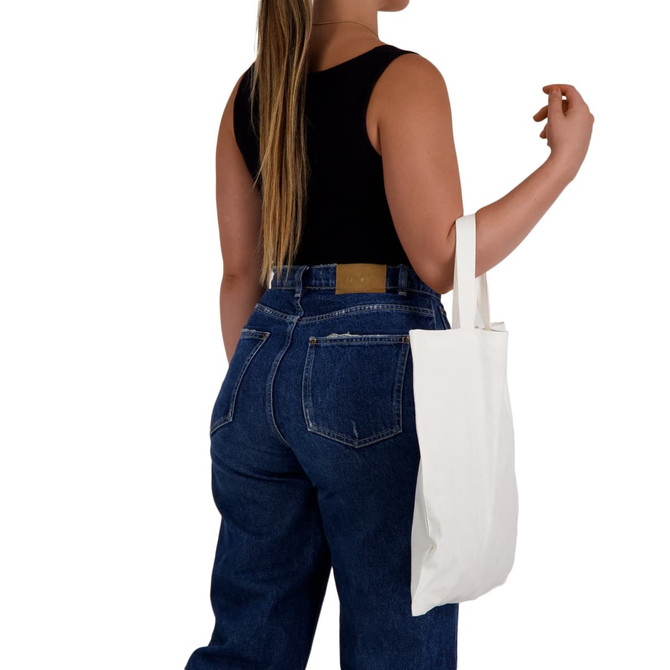A woman holding a white short handle bamboo tote bag, wearing a black top and blue jeans. The bag has a simple design and a logo.
