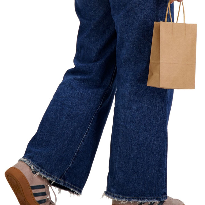 A small brown paper bag is held by a person dressed in blue denim jeans and tan platform shoes.