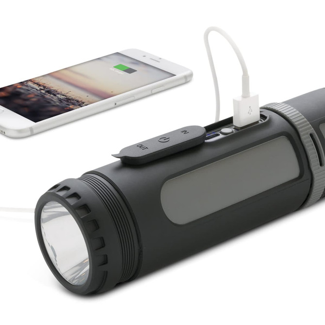 A black 4-in-1 speaker resembling a flashlight, with a charging port and a smartphone connected for charging.