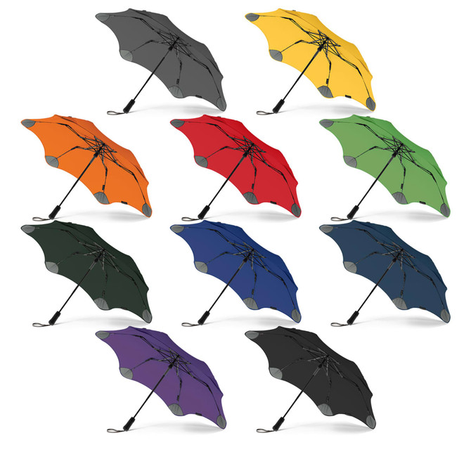 A collection of BLUNT Metro Umbrellas in various colours, including grey, orange, yellow, green, red, black, blue, and purple.