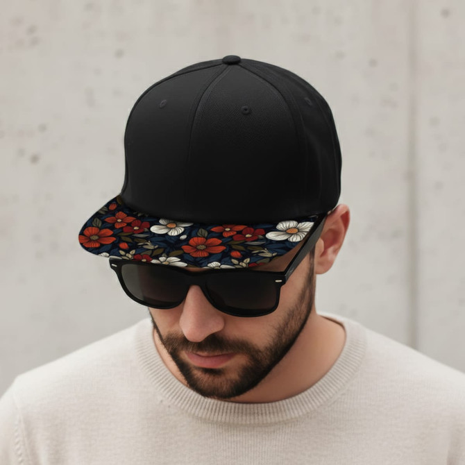 A black flat peak cap with a floral-patterned brim, worn by a man in sunglasses and a light-coloured sweater.