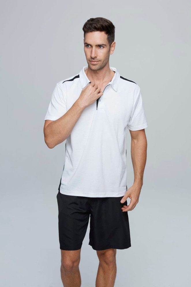 A man wearing a white polo shirt with black accents, paired with black shorts, featuring a logo.