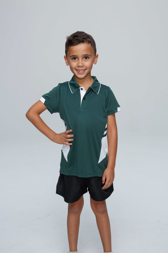 A young boy poses in a green polo shirt with white accents, paired with black shorts. It features a logo on the chest.