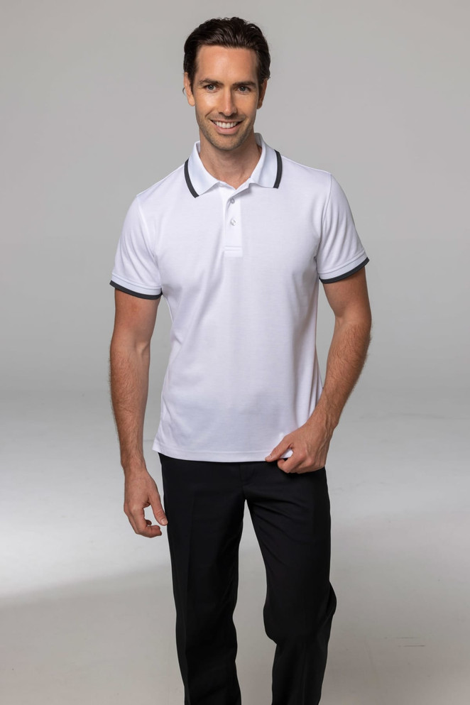 A man wearing a white polo shirt with black trim, paired with dark trousers, standing against a neutral background.